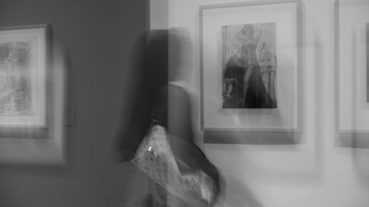 Blurred motion of a woman observing artwork in a gallery, creating an abstract effect.